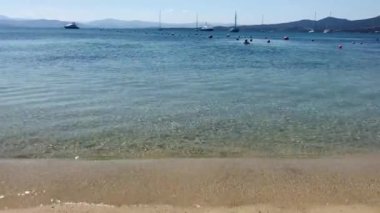 Sessiz deniz dalgaları açık bir günde kumda koşar. Dağın ufuklarında, yatlarda, bir adam yüzer