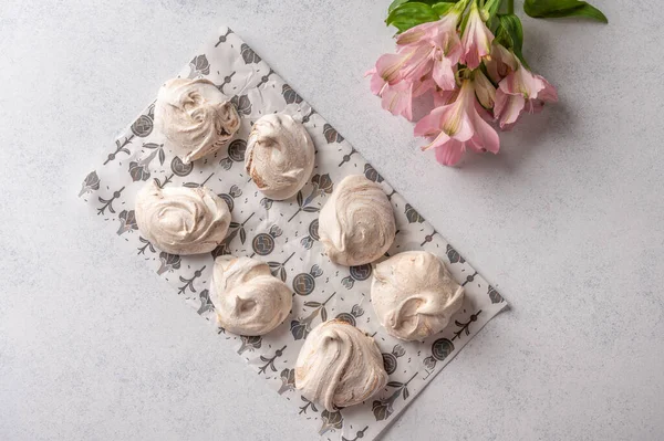 Homemade popular eggs dessert meringue on a pastry paper on light background. Next to pink flower. Copy space