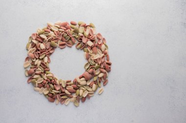 Multi-colored pasta shells in the shape of a circle with space in the middle on a gray textured background. Healthy food concept