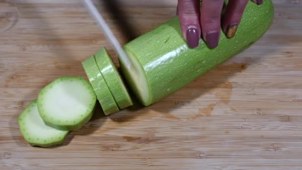 Woman cuts fresh zucchini into slices with ceramic knife on a wooden cutting board. Close up — Stock Video