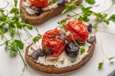 Beyaz seramik tabakta ev yapımı domatesli, zeytinli, peynirli ve otlu sandviçler.