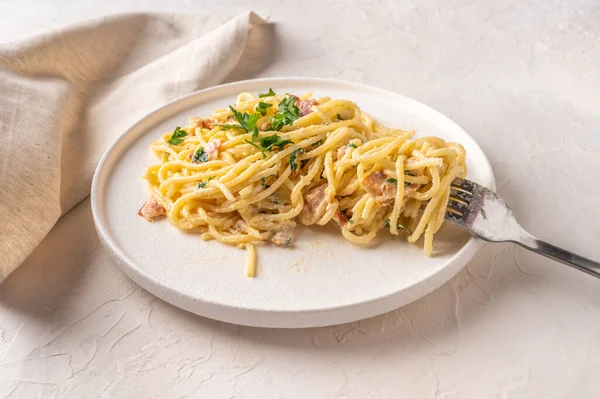 Carbonara classica fatta in casa con pancetta, uova, parmigiano su piatto leggero in ceramica con forchetta e tovagliolo su tavolo leggero. Vista da vicino — Foto Stock