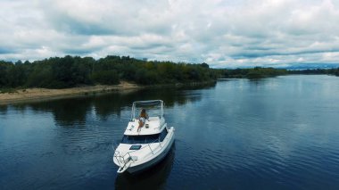 Sıcak yaz gününde motorlu tekneyle güzel mavi göl manzarası. Güzel genç kadın güvertedeki yatta dinleniyor, yürüyor ve öpüşüyor.