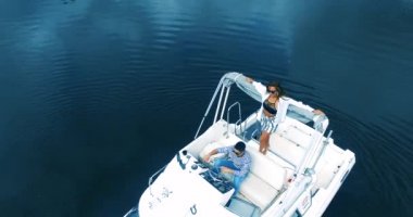Sıcak yaz gününde motorlu tekneyle güzel mavi göl manzarası. Güzel genç kadın güvertedeki yatta dinleniyor, yürüyor ve öpüşüyor.