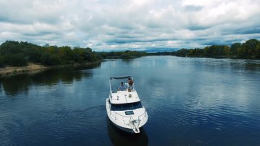Sıcak yaz gününde motorlu tekneyle güzel mavi göl manzarası. Güzel genç kadın güvertedeki yatta dinleniyor, yürüyor ve öpüşüyor.