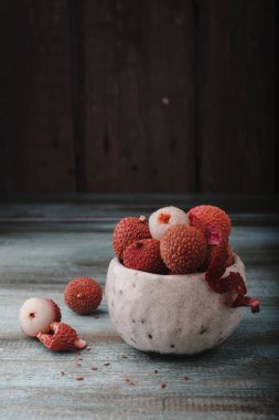 Kopyalama alanı olan Litchi chinensis. Eski ahşap arka planda bir kasede taze litchi meyveleri. Çiğ kırmızı organik liçi meyvesi yemeye hazır..