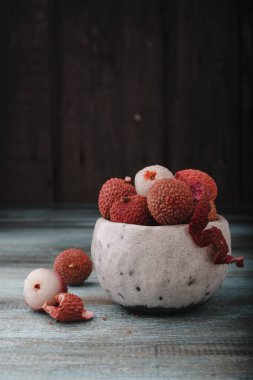 Kopyalama alanı olan Litchi chinensis. Eski ahşap arka planda bir kasede taze litchi meyveleri. Çiğ kırmızı organik liçi meyvesi yemeye hazır..