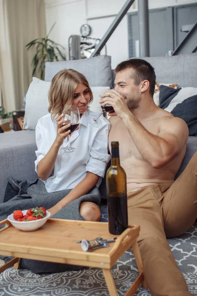 Young man smiling to his gorgeous woman while have romantic dinner and drinking wine on valentines day. Leisure, celebration and honeymoon concept - happy couple drinking red wine at home in evening