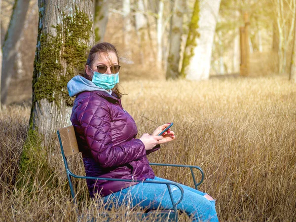 Sad Woman sitting alone on bench in park wearing face mask to avoid infectious. Corona virus, or Covid 19, is spreading all over the world.