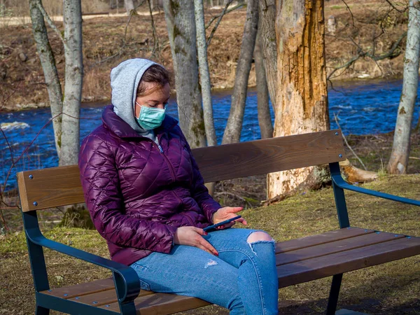 Sad Woman sitting alone on bench in park wearing face mask to avoid infectious. Corona virus, or Covid 19, is spreading all over the world.