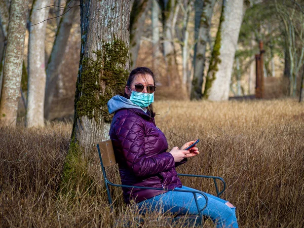 Sad Woman sitting alone on bench in park wearing face mask to avoid infectious. Corona virus, or Covid 19, is spreading all over the world.