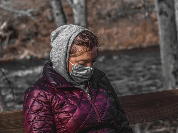 悲しい女性は 感染を避けるために顔面マスクを着用して公園のベンチに一人で座っています コロナウイルス またはコビド19は世界中に広がっています — ストック写真