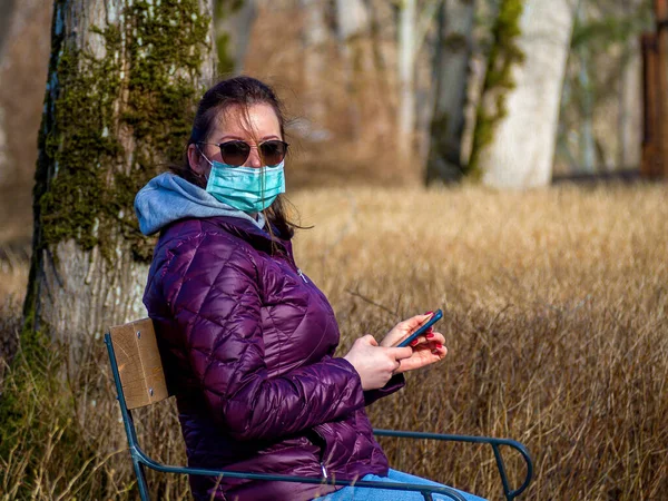 Sad Woman sitting alone on bench in park wearing face mask to avoid infectious. Corona virus, or Covid 19, is spreading all over the world.