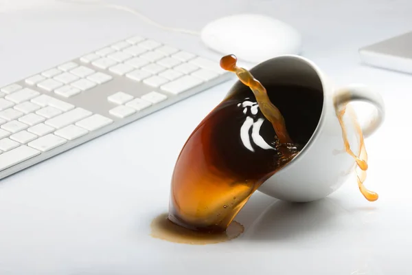 Falling and spilling of a cup of coffee on top of a desk with a computer