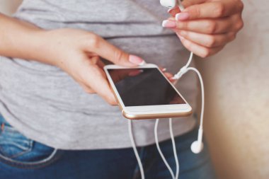 Bir akıllı telefon telleri kulaklık üzerinden ile tutan genç bir kadın eli