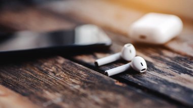 Smartphone and wireless earphones with case, close up isolated on the wooden background. 