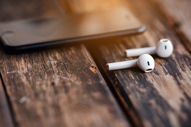 Smartphone and wireless earphones, close up isolated on the wooden background. 