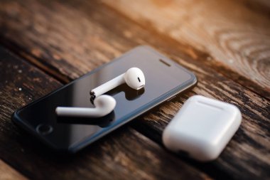 Smartphone and wireless earphones, close up isolated on the wooden background. 