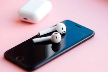Pembe arka planda izole edilmiş akıllı telefon ve kablosuz kulaklıklar.. 