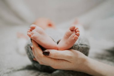 Anne, bebeğin ayaklarını elinde tutuyor.