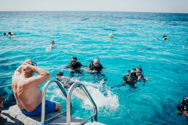 Maskeli insanlar kızıl denizde yüzer.