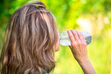 blonde lady drinking  bottled water outside clipart