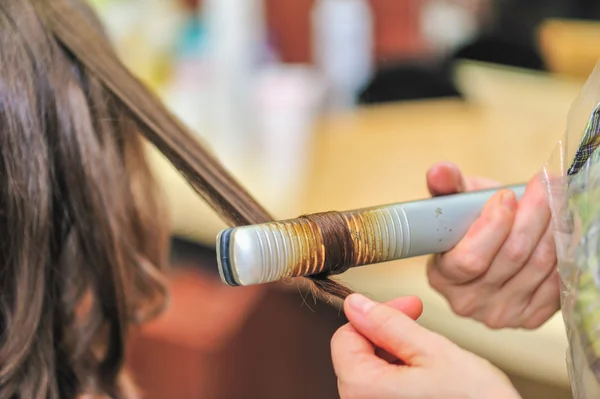 Primo piano di un parrucchiere che raddrizza capelli castani lunghi con ferri da stiro per capelli . — Foto Stock