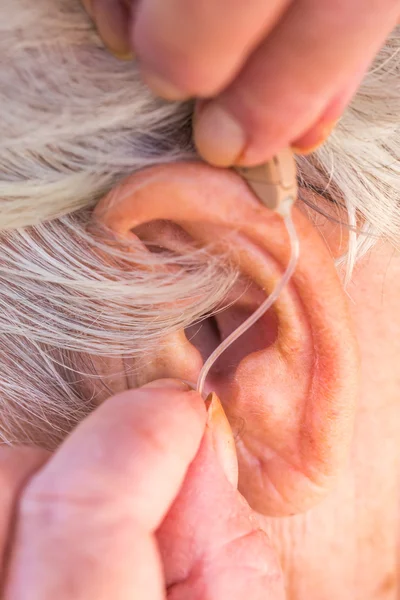 Пожилая женщина вставляет слуховой аппарат ей в уши — стоковое фото