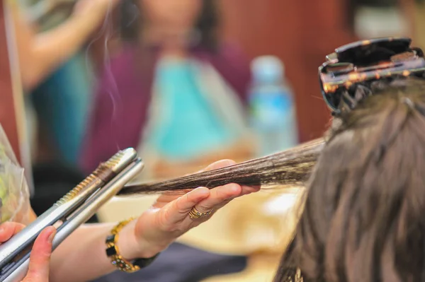 Крупный план парикмахера, выпрямляющего длинные каштановые волосы утюгами . — стоковое фото