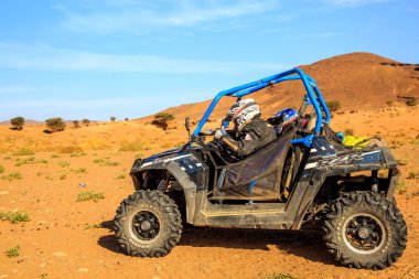 Merzouga, Morocco - Feb 26, 2016: Blue Polaris RZR 800 and pilots in Morocco desert near Merzouga. Merzouga is a small village located in the Saharan south-eastern Morocco. Merzouga is famous for its  clipart