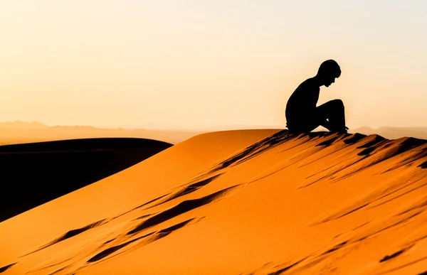 Meditando giovane seduto su una duna di sahara — Foto Stock