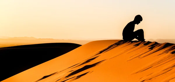 Медитирующий молодой человек, сидящий на вершине дюны Сахары — стоковое фото