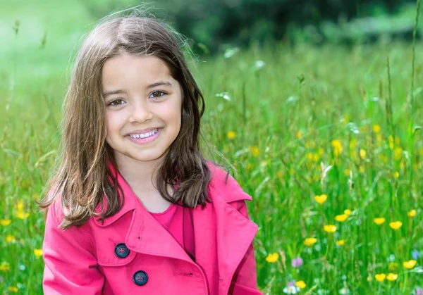 Glückliches süßes Kind, das im Gras eines Blumengartens sitzt — Stockfoto