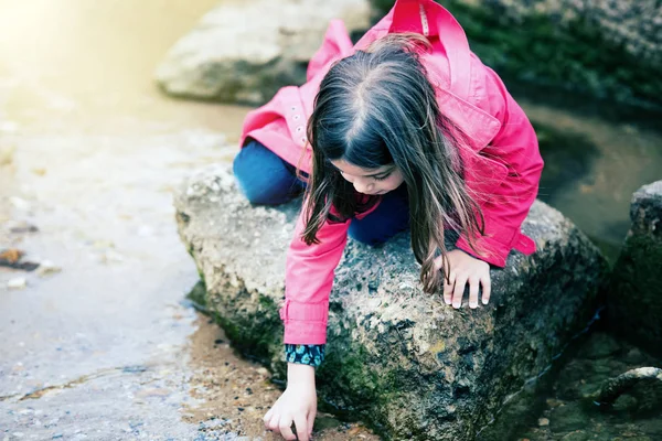 Bonita niña jugando en una roca en el borde del agua — Foto de Stock