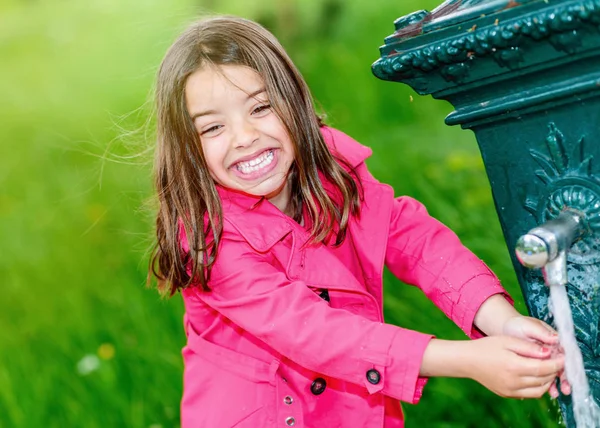 Kleines Mädchen trinkt Wasser in einem Brunnen — Stockfoto