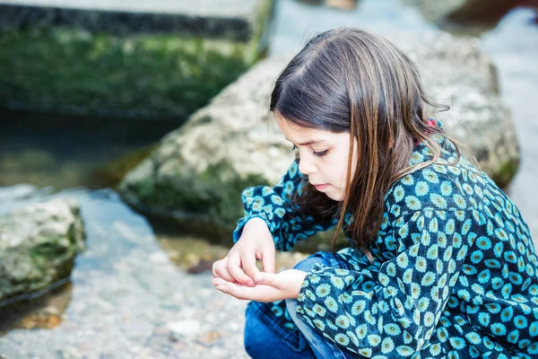 漂亮的小女孩在玩一块岩石在水的边缘 — 图库照片