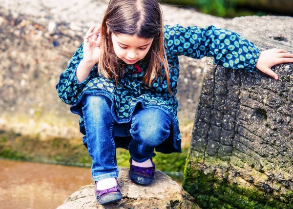 Hübsches kleines Mädchen spielt auf einem Felsen am Ufer des Wassers — Stockfoto
