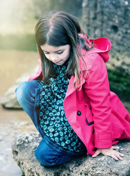 Hübsches kleines Mädchen spielt auf einem Felsen am Ufer des Wassers — Stockfoto