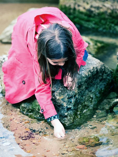 Bonita niña jugando en una roca en el borde del agua — Foto de Stock