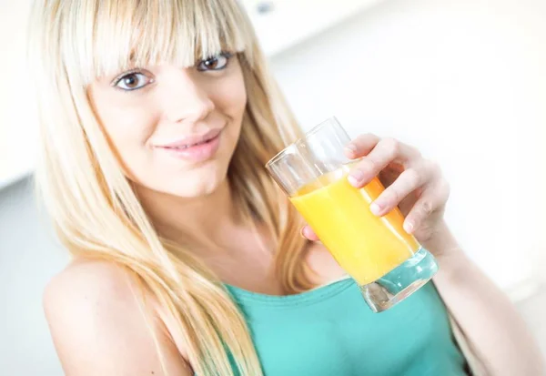 Aantrekkelijk meisje een oranje drinken in een keuken — Stockfoto