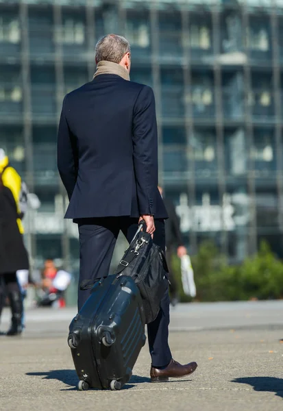 La defense, France- 09 апреля 2014 года: зрелый бизнесмен, идущий по улице и вытаскивающий чемодан — стоковое фото