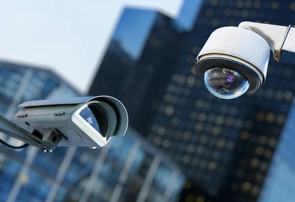 Due telecamere di sicurezza cctv in una città con blury business building sullo sfondo — Foto Stock