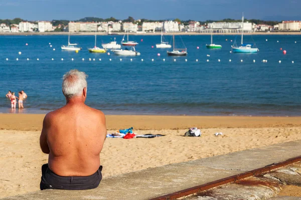 Сибур, Франция - 26 сентября 2016 года: пляж Сибур с пенсионером, сидящим сзади на переднем плане, и залив Сен-Жан-де-Луз с лодками на заднем плане — стоковое фото