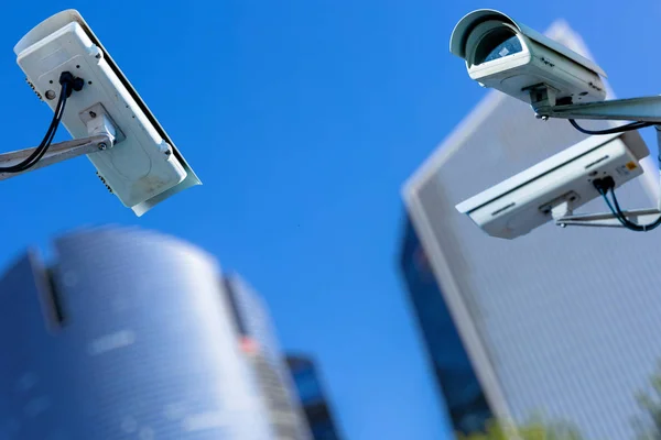 Due telecamere di sicurezza cctv in una città con blury business building sullo sfondo — Foto Stock