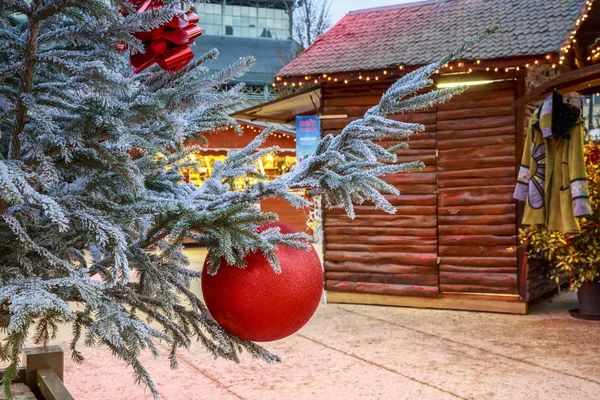 Niort, Francia - 05 dicembre 2017: Primo piano di una palla di Natale appesa ad un albero di neve con gli chalet del mercatino di Natale sullo sfondo — Foto Stock