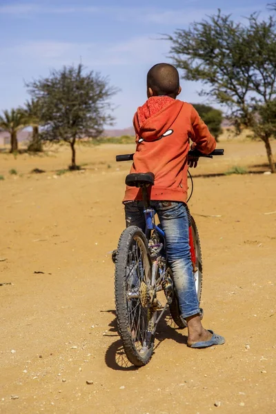 Tinzouline, Marrocos - 26 de fevereiro de 2016: Vista traseira do menino marroquino andando de bicicleta no deserto na aldeia Tinzouline, em Marrocos — Fotografia de Stock