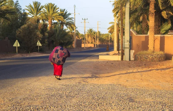 M'hamid, Morocco - February 22 2016: Woman carrying jute burlap sack during evening — Stock Photo, Image