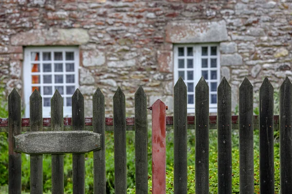 En ganska sten stuga med sten överliggare och vita spröjsade fönster står omgiven av gräs och ett staket. — Stockfoto