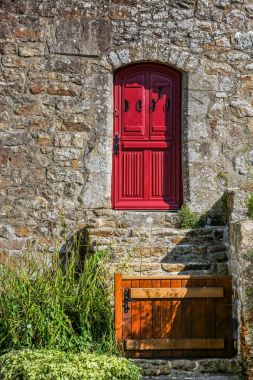 Ahşap bir bariyer ve kırmızı bir kapı ile eski taş ev