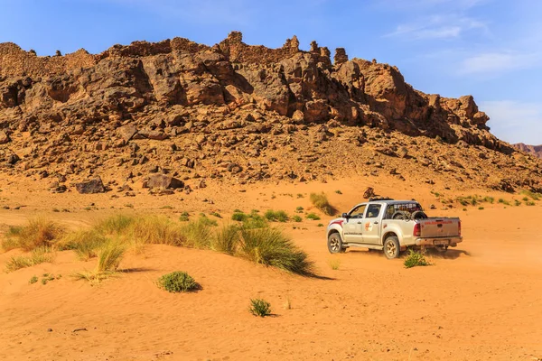 SUV kör under en stenig kulle i den marockanska öknen på en solig dag — Stockfoto